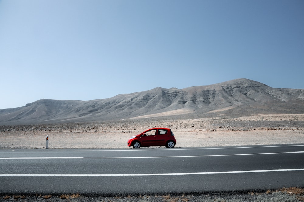 a red car driving down a desert road