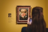 a woman taking a picture of a painting on a wall