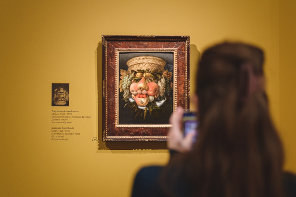 a woman taking a picture of a painting on a wall