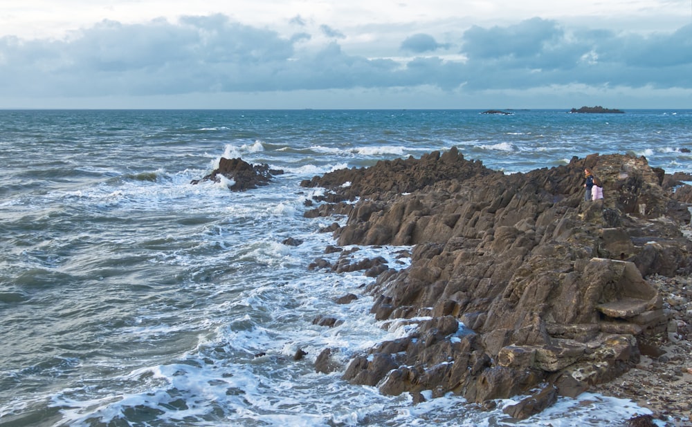 a couple of people standing on top of a rocky beach