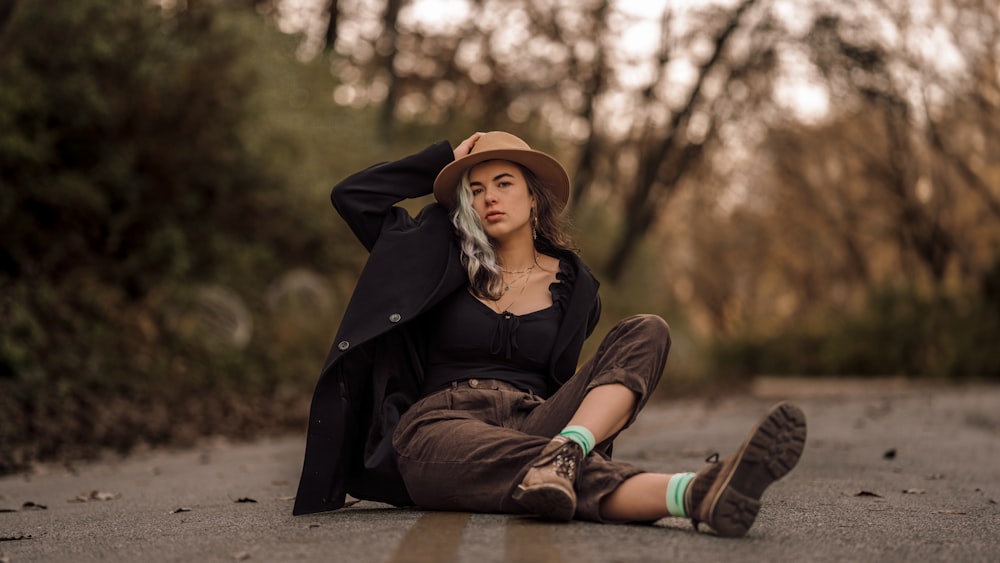 a woman sitting on the side of a road wearing a hat