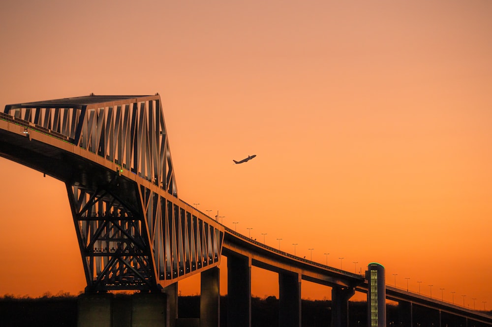 an airplane is flying over a bridge at sunset