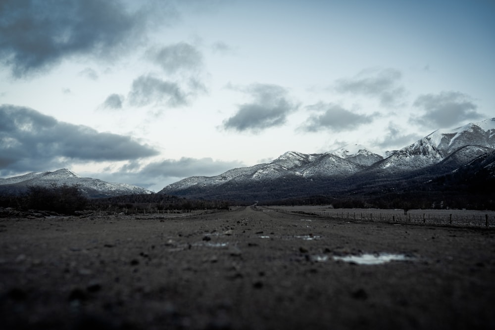 a dirt road surrounded by mountains under a cloudy sky