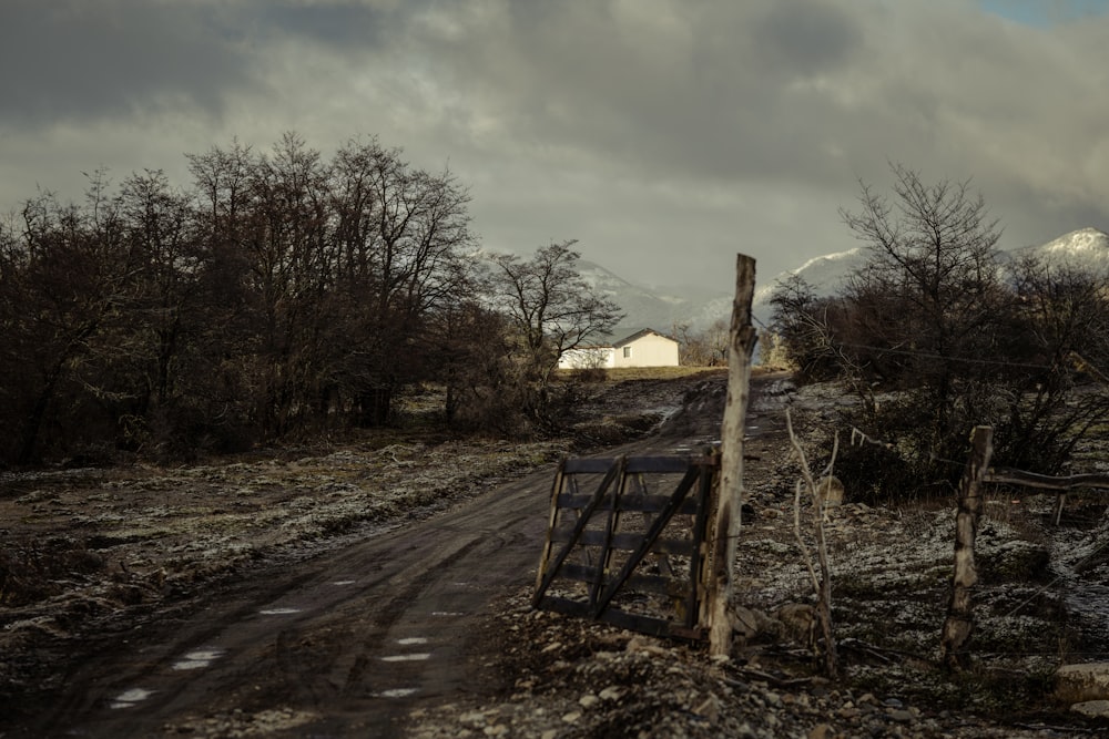 a dirt road with a fence and a house in the background