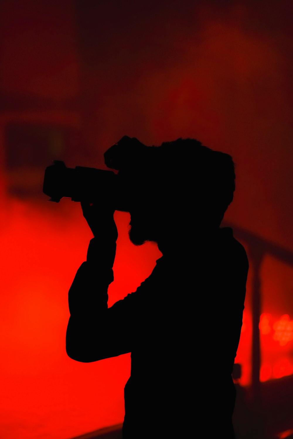 a silhouette of a man holding a camera in front of a red background