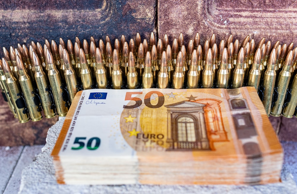 a bunch of bullet shells sitting on top of a pile of 50 euros bills