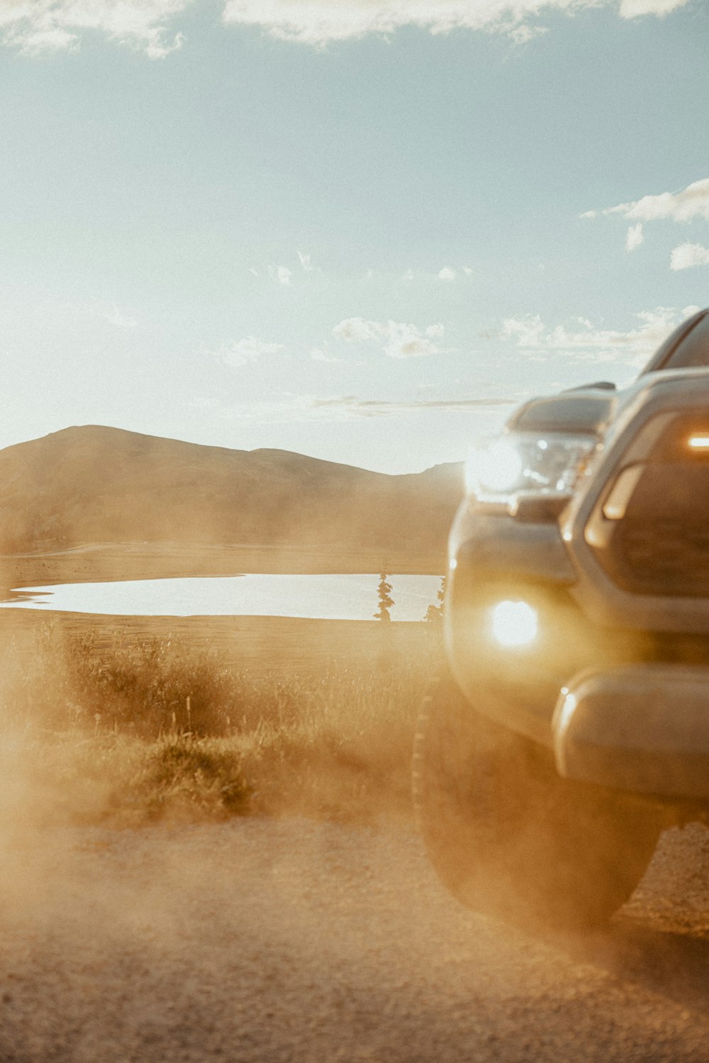 a truck driving down a dirt road next to a lake