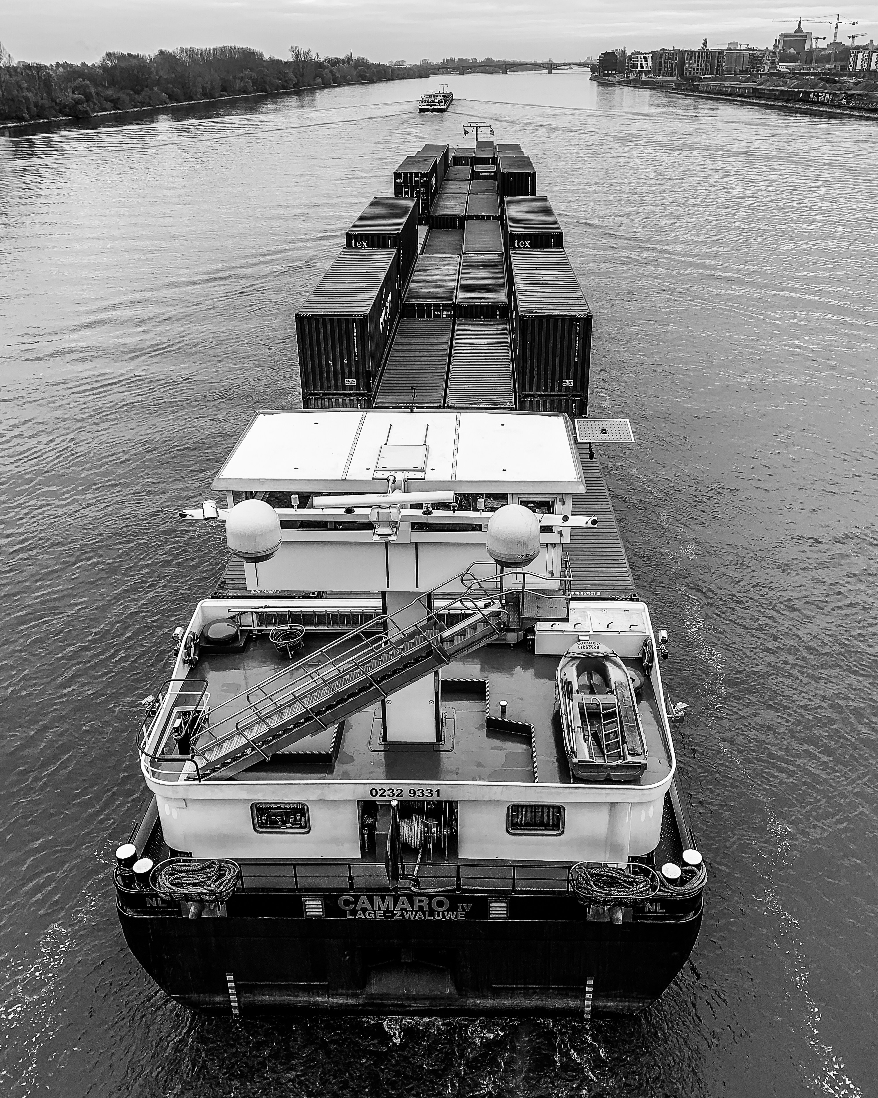 Large dredging vessel operating in a wide river channel, murky brown water, industrial port infrastructure in background, overcast sky
