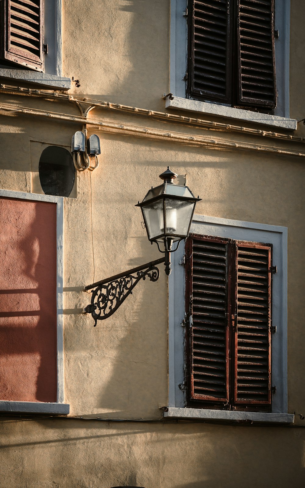 a lamp on the side of a building with shutters open