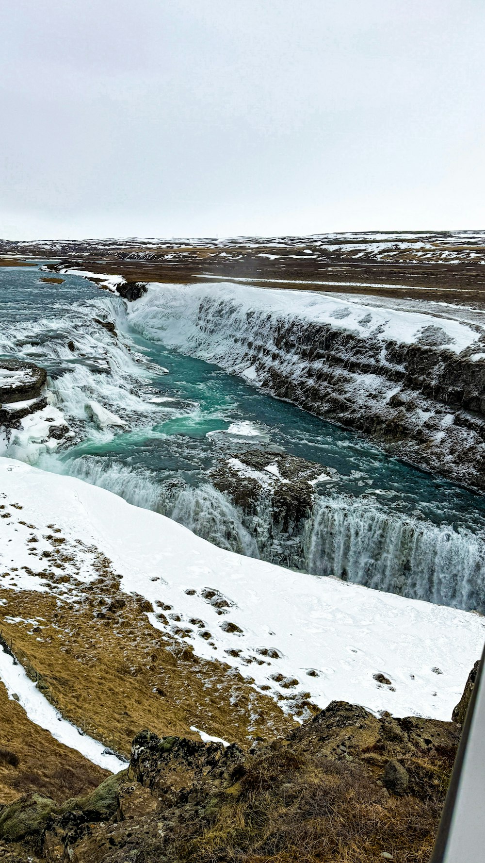 a man standing on top of a snow covered hill next to a waterfall