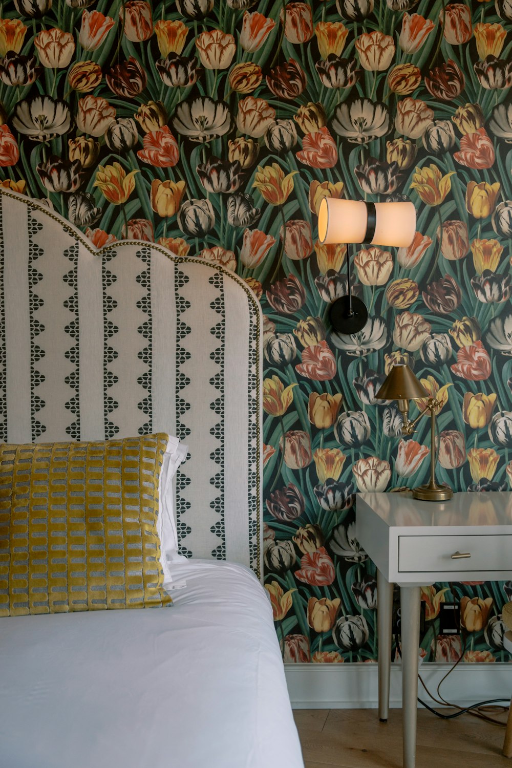 a bed sitting next to a white table with a lamp on top of it