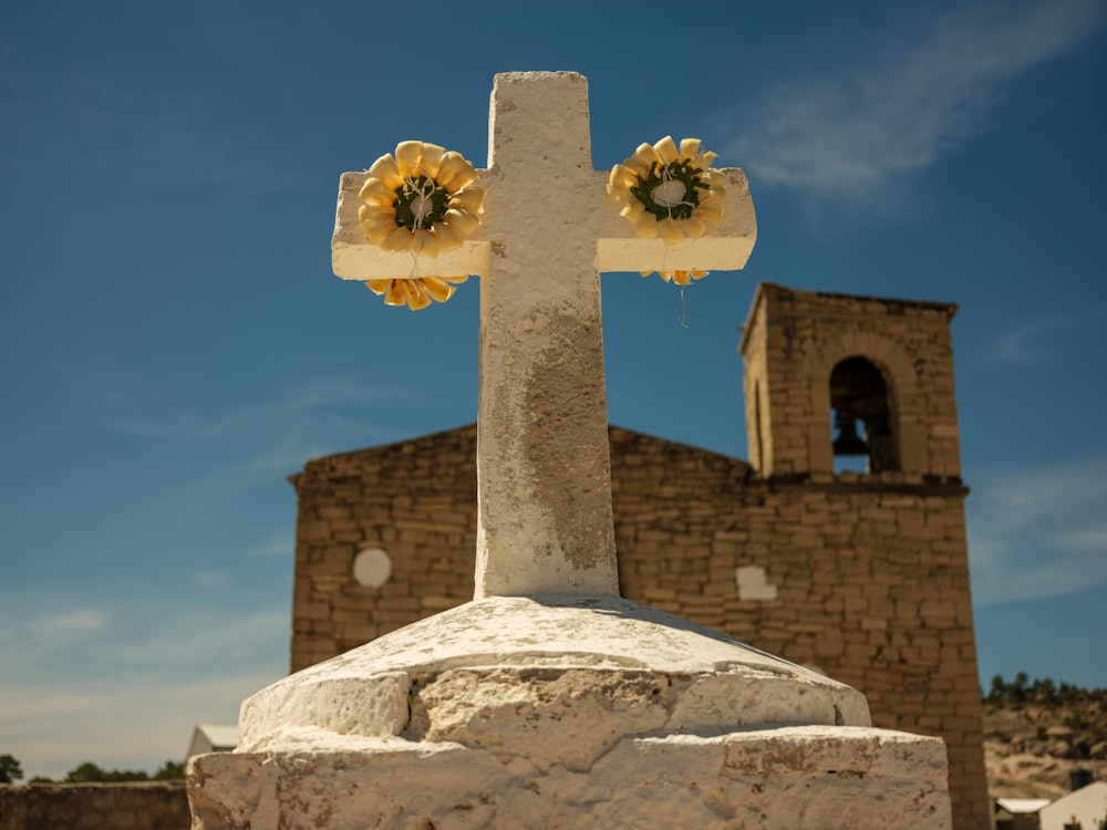 a stone cross with flowers on it in front of a church