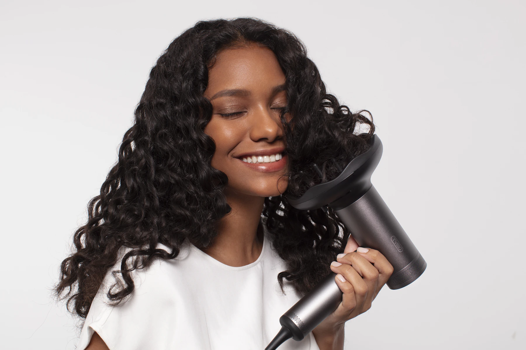 A person styling curly hair with an electric hair dryer