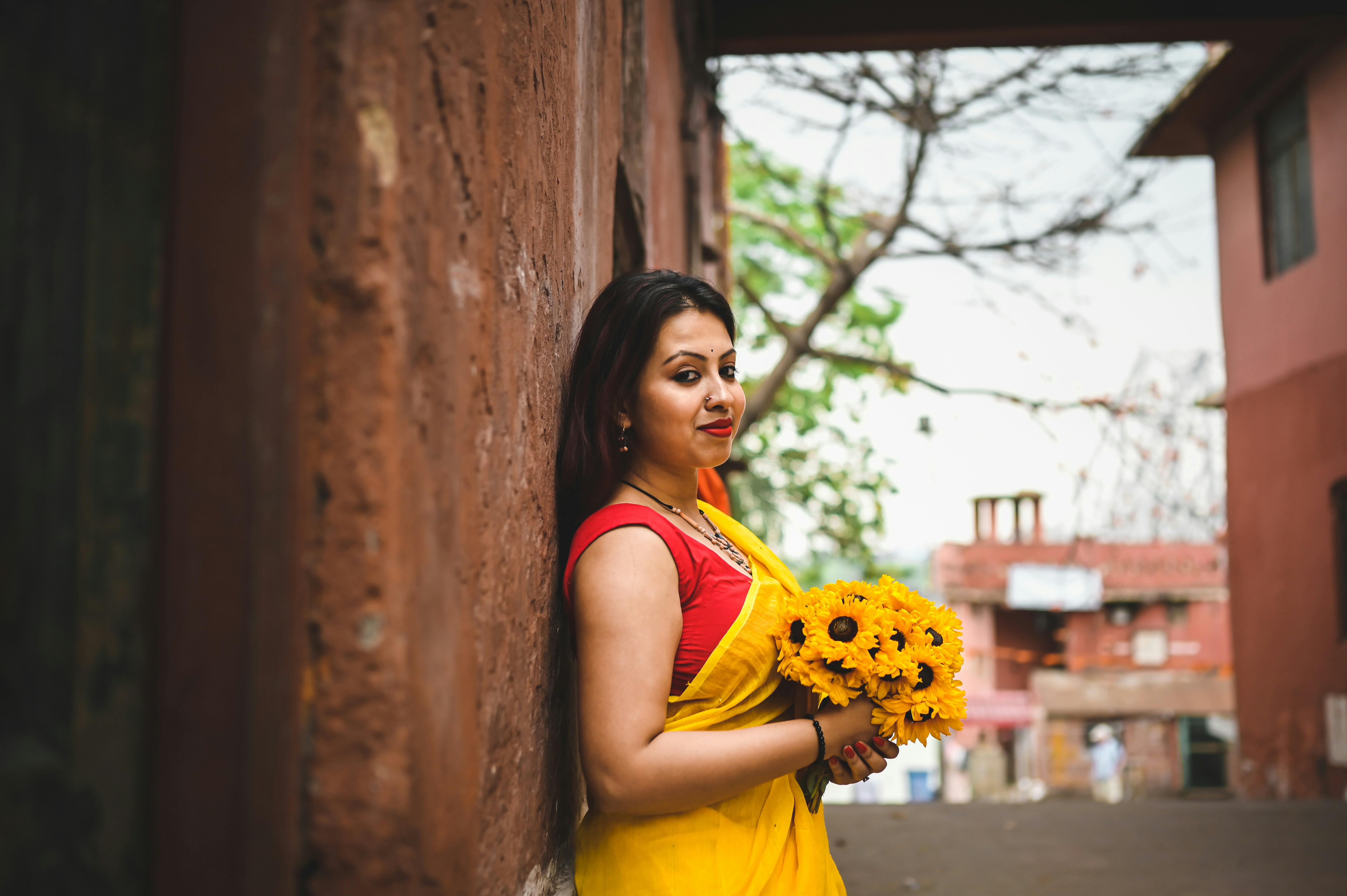a woman leaning against a wall holding flowers