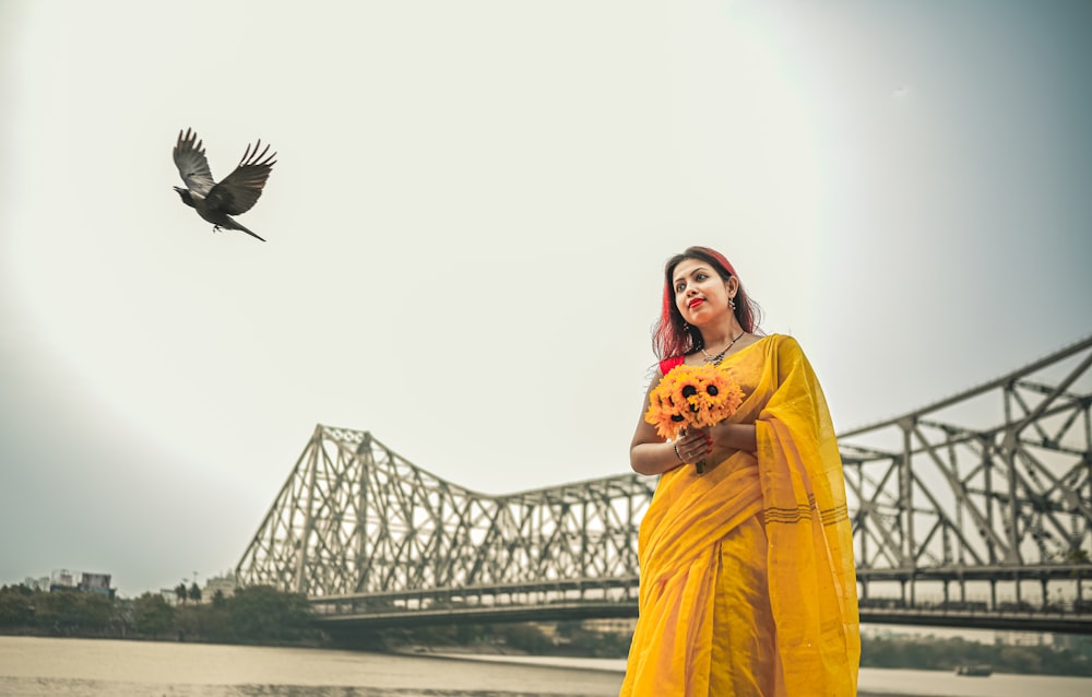 a woman in a yellow sari and a bird flying in the sky