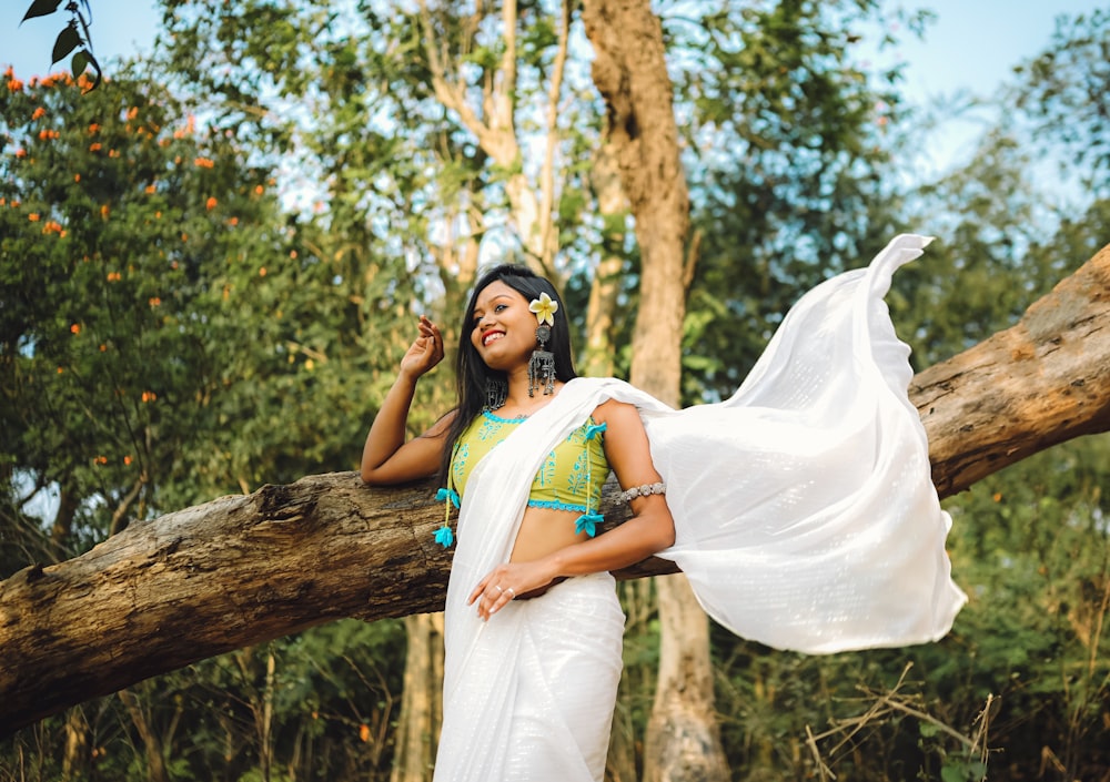 a woman in a white sari standing next to a tree
