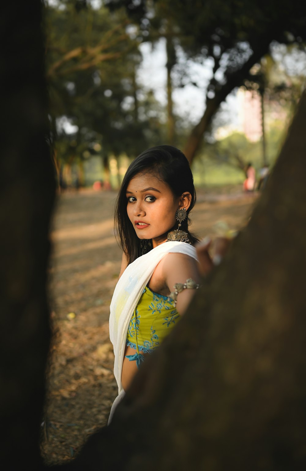 a beautiful young woman standing next to a tree