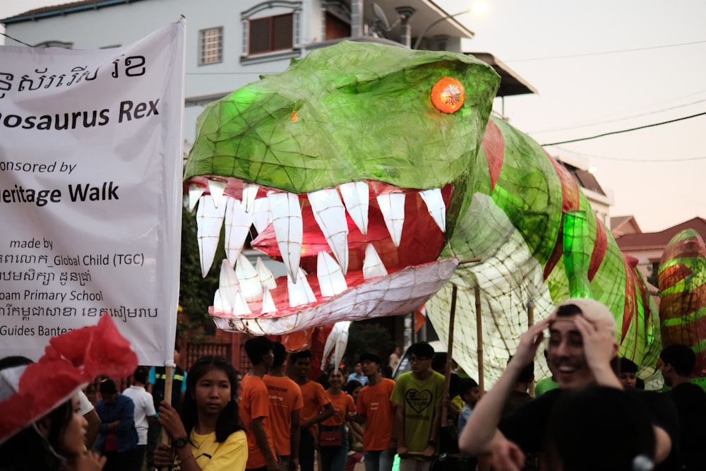 a group of people walking down a street next to a green dragon