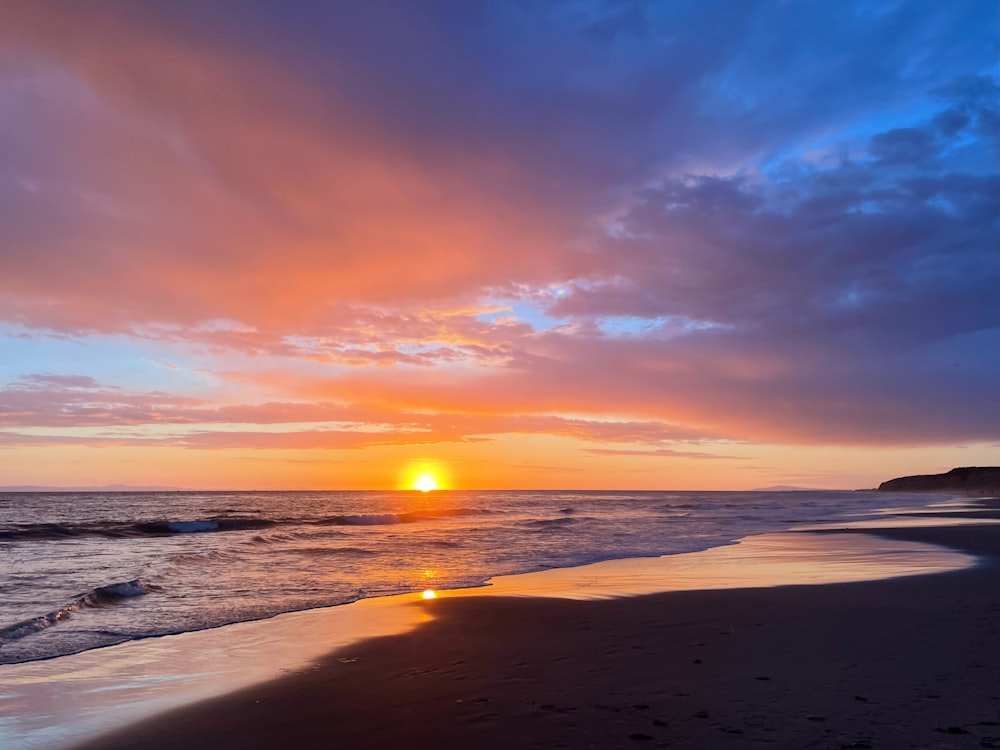 the sun is setting over the ocean on the beach