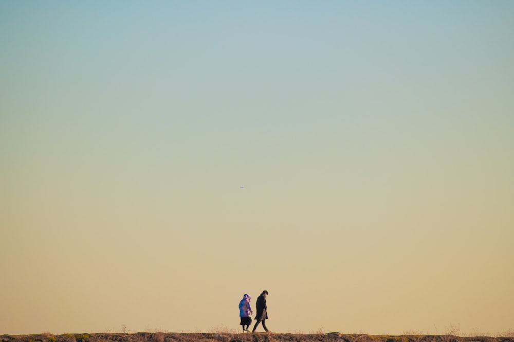 a couple of people walking across a dry grass field
