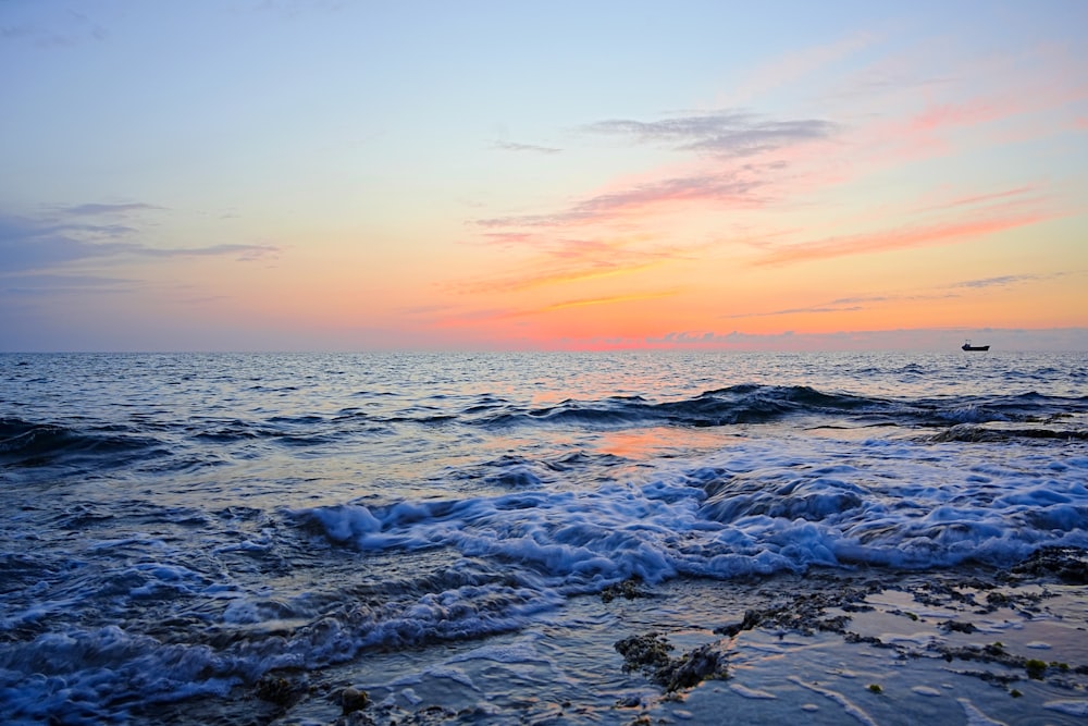 a sunset over the ocean with a boat in the distance