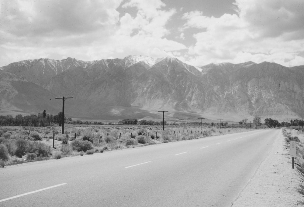 a black and white photo of a road with mountains in the background
