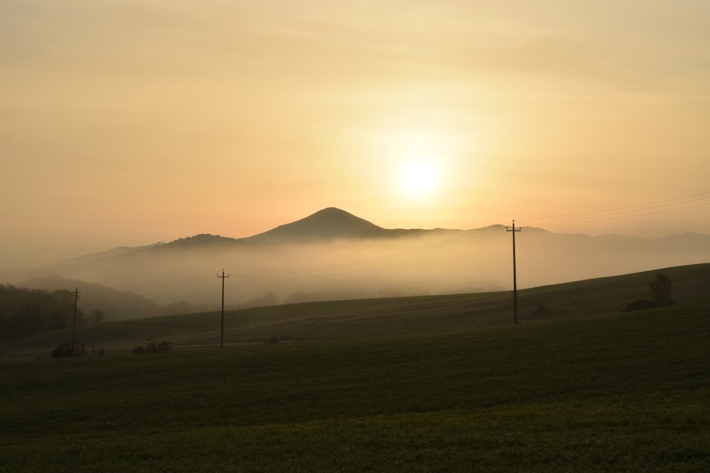 the sun is setting over a grassy hill