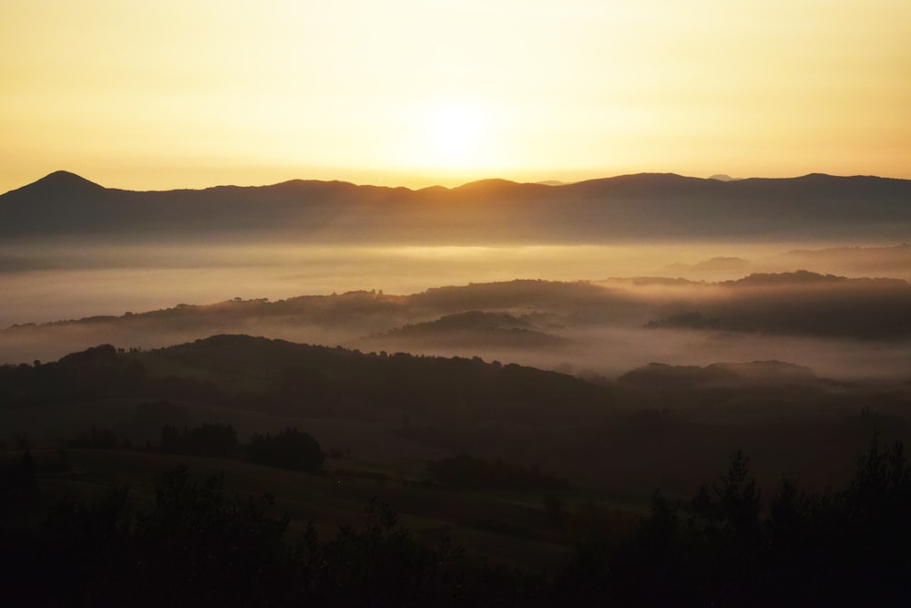 the sun is setting over the mountains covered in fog