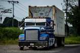 a blue semi truck driving down a rural road