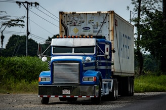 a blue semi truck driving down a rural road