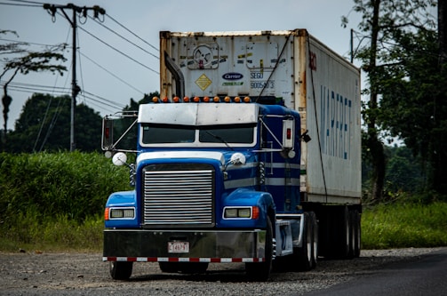 a blue semi truck driving down a rural road