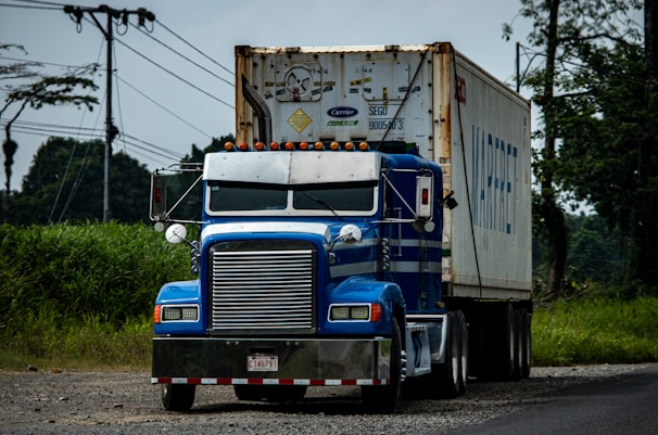 a blue semi truck driving down a rural road