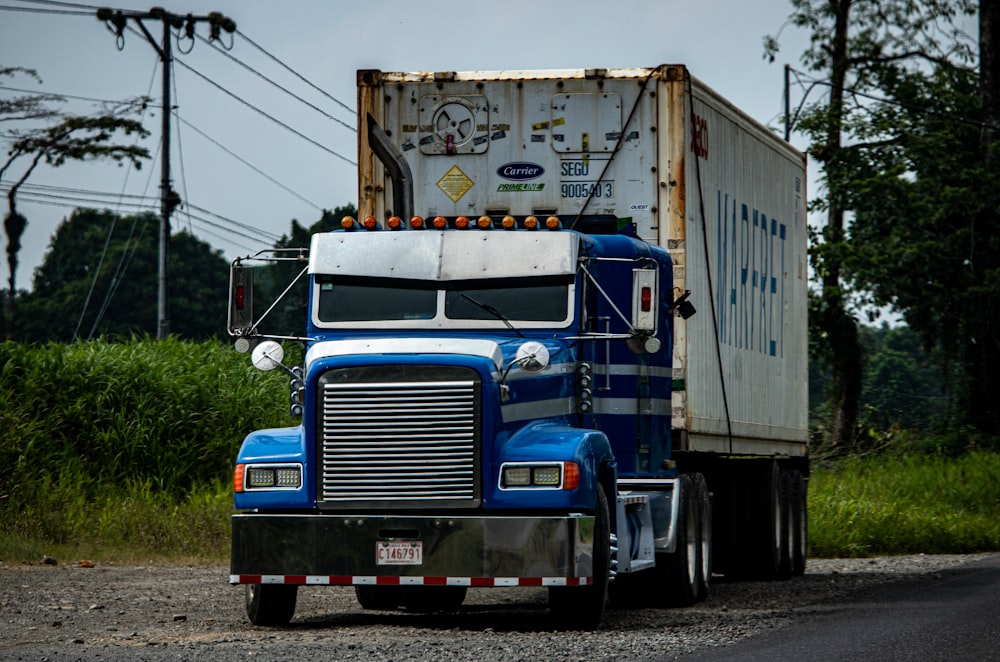 a blue semi truck driving down a rural road