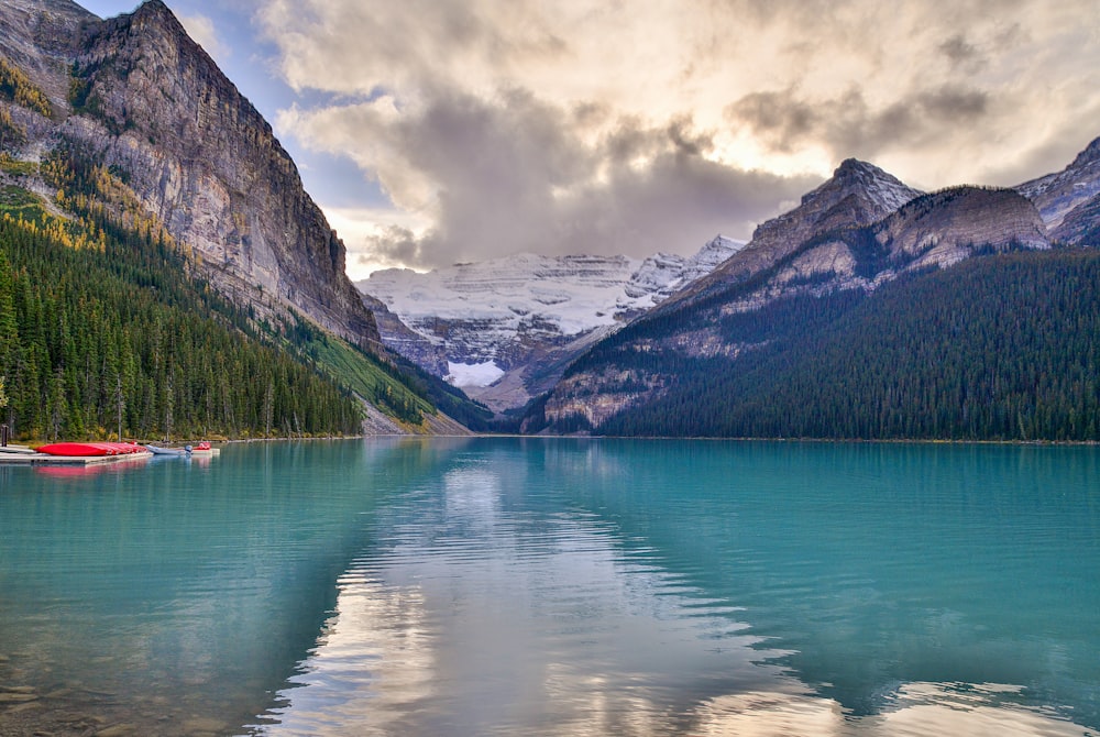 a lake surrounded by mountains under a cloudy sky