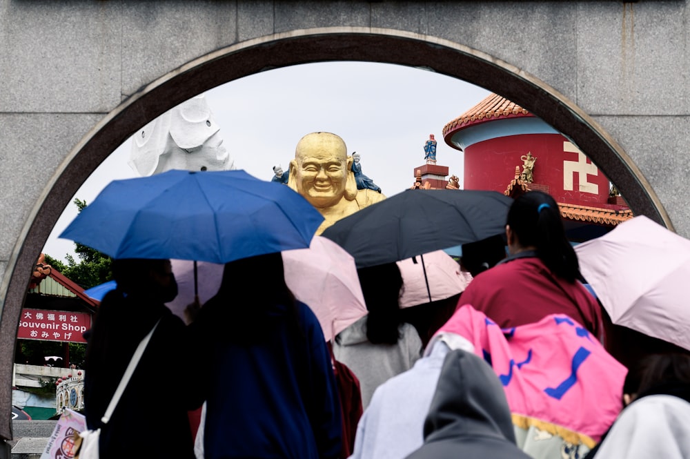 a group of people with umbrellas standing in front of a buddha statue