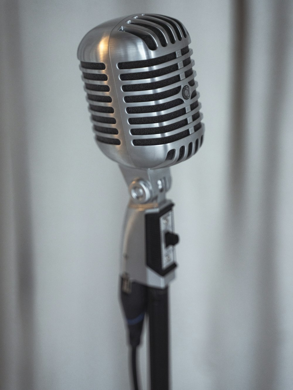 a silver microphone with a black stand and a white curtain behind it