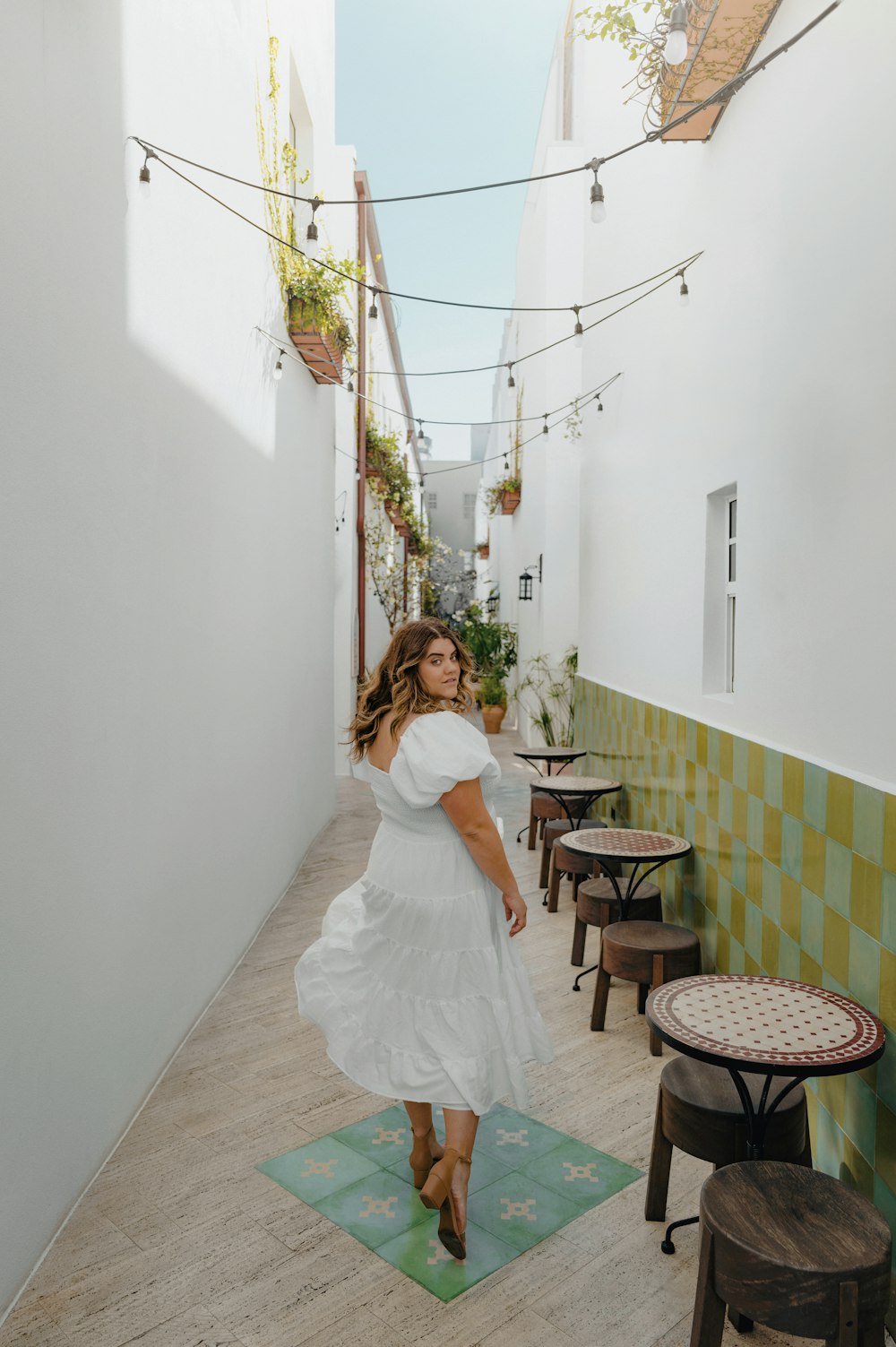 a woman in a white dress is walking down a narrow alleyway
