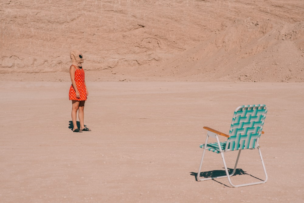 a woman in an orange dress standing next to a blue lawn chair