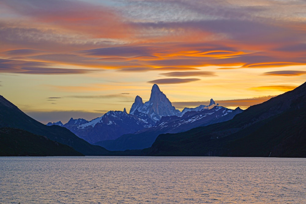 a mountain range is silhouetted against a sunset over a body of water