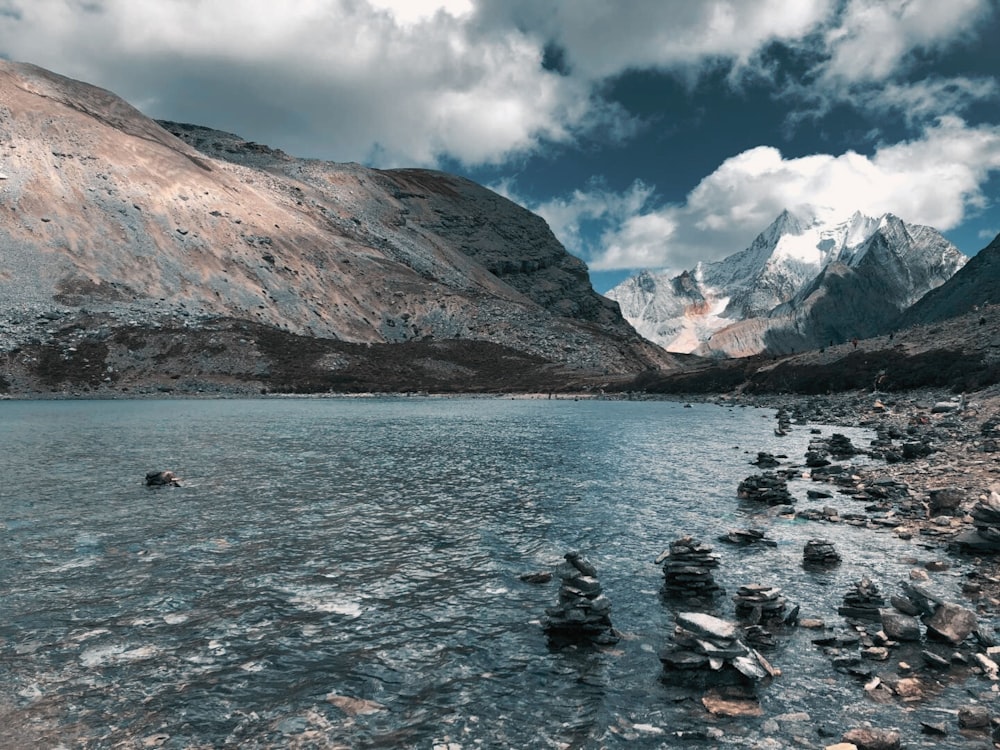 um lago cercado por montanhas e rochas sob um céu nublado