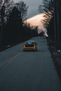 a yellow car driving down a road next to a forest