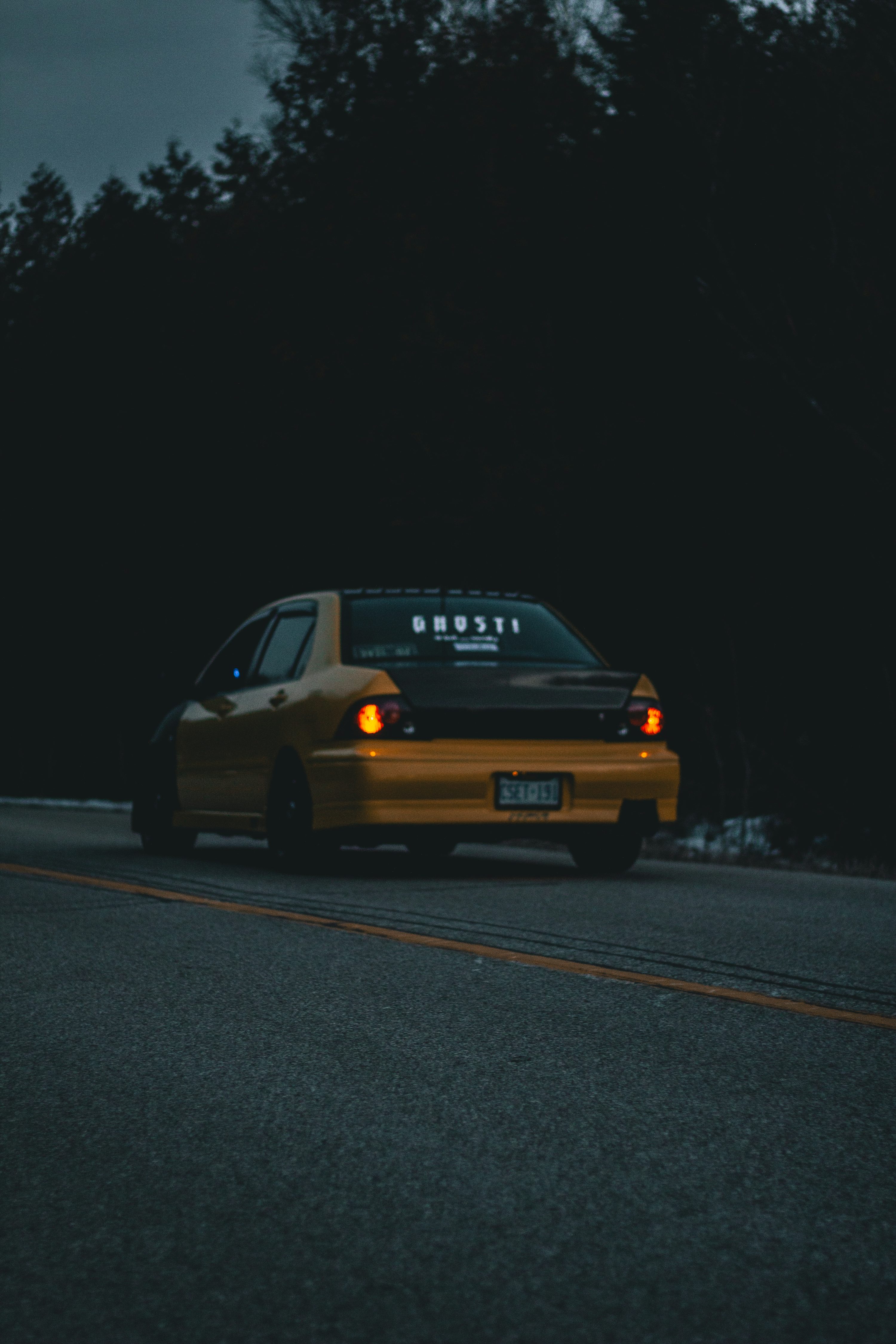 a yellow taxi driving down a street next to a forest