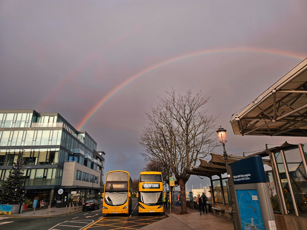 a double decker bus parked in front of a building with a rainbow in the sky