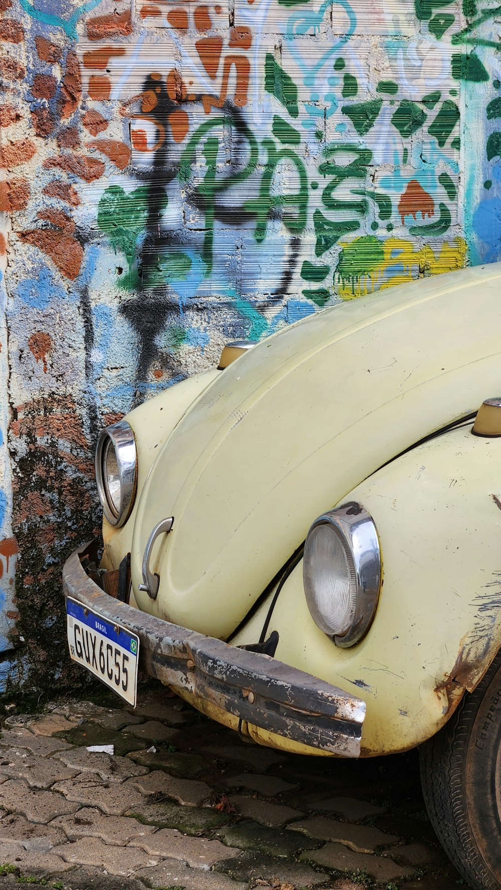 an old yellow vw bug parked in front of a graffiti covered wall