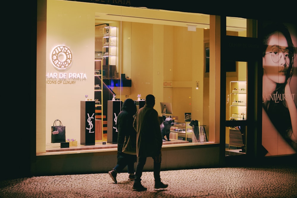 two people walking past a store front at night