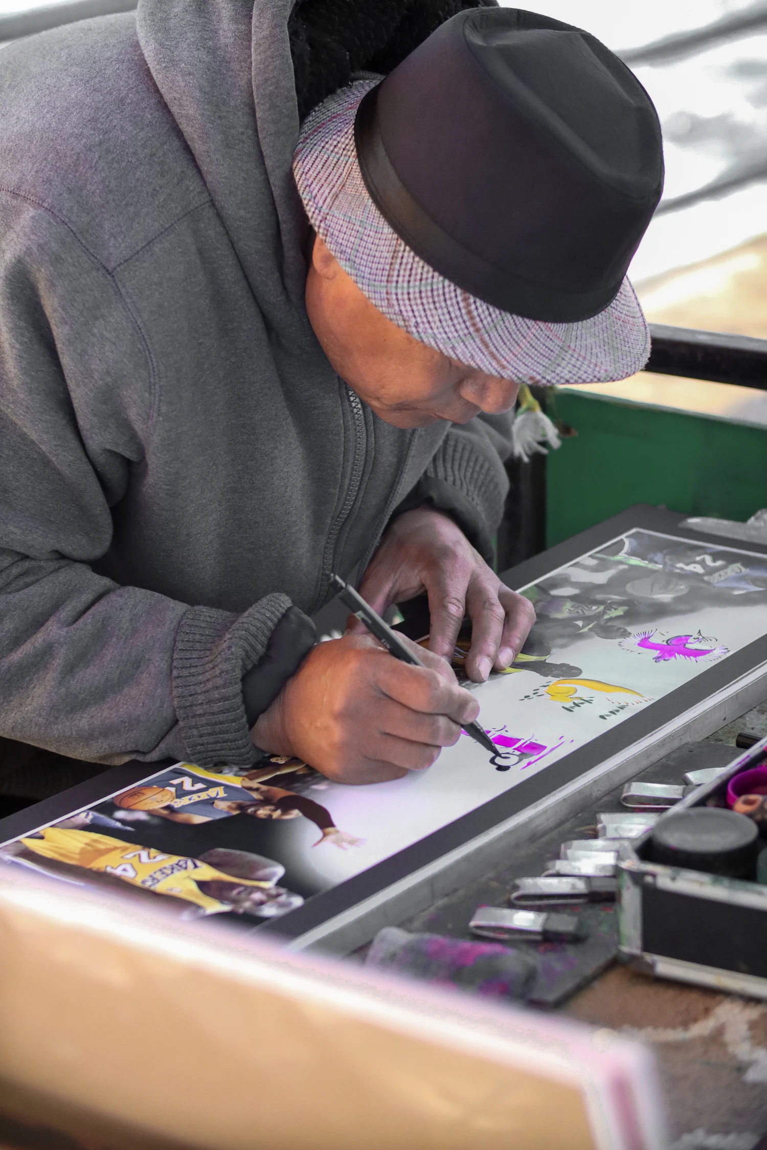 Corsin Kläy in a grey hat bent over a colourful drawing at his desk