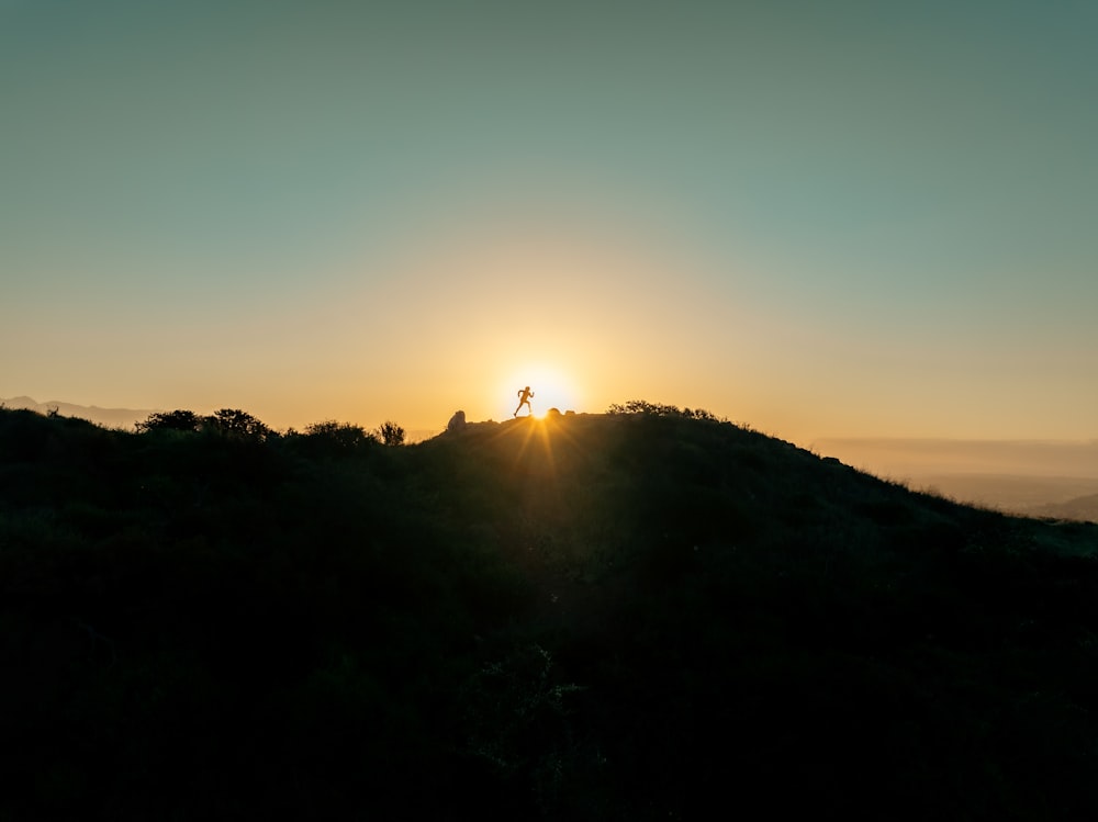 the sun is setting over a hill with a person on it