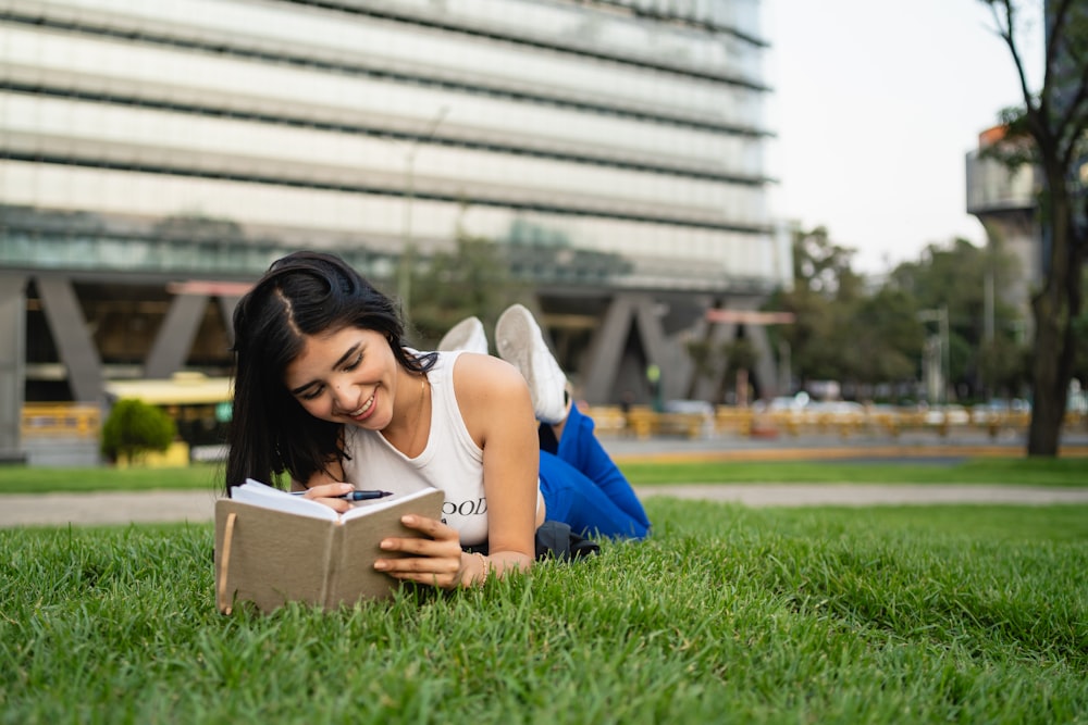 a woman laying on the grass reading a book