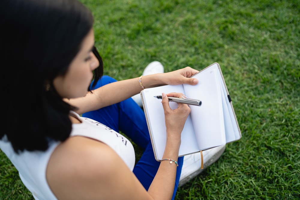 a woman sitting in the grass writing on a notebook