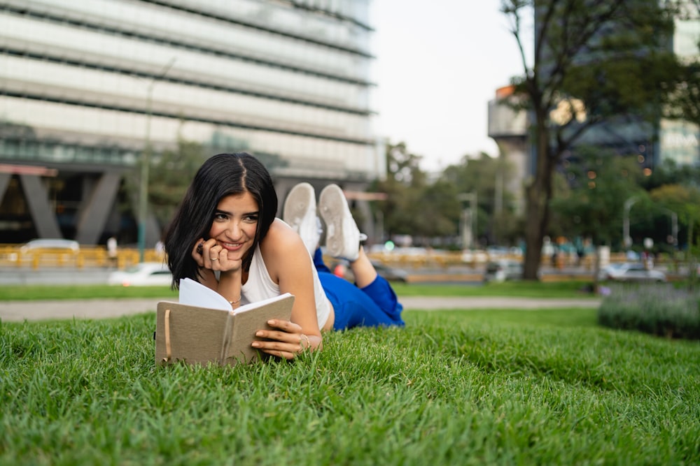 a woman laying on the grass reading a book